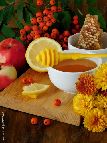 Honey, lemon and rowan berries surrounded by flowers on a wooden board