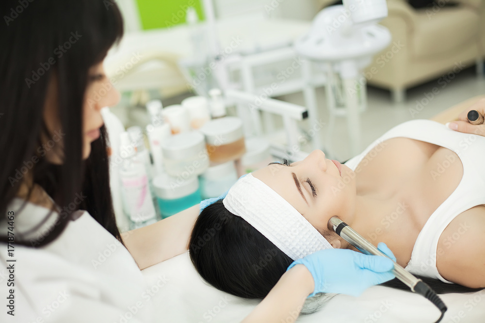 Doctor with Ultrasonic scraber. Doing procedure of ultrasonic cleaning of face. Model, profile. Cosmetological clinic. Patient. Healthcare, clinic, cosmetology. Doctor with Ultrasonic scraber. Doing procedure of ultrasonic cleaning of face. Model, profile. Cosmetological clinic. Patient. Healthcare, clinic, cosmetology.