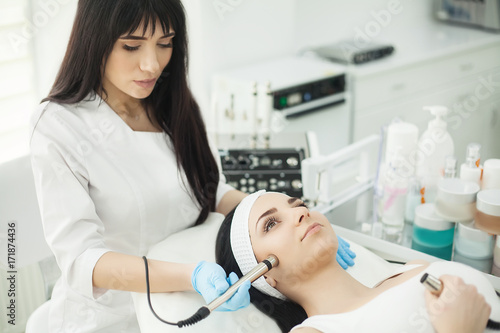 Doctor with Ultrasonic scraber. Doing procedure of ultrasonic cleaning of face. Model, profile. Cosmetological clinic. Patient. Healthcare, clinic, cosmetology.