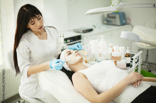 Woman lying on massage table in health spa while facial mask is applied on her face