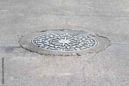 Manhole cover on the street surrounded by asphalt.