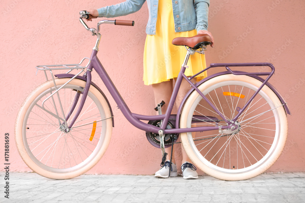Obraz premium Beautiful young woman with bicycle on color wall background