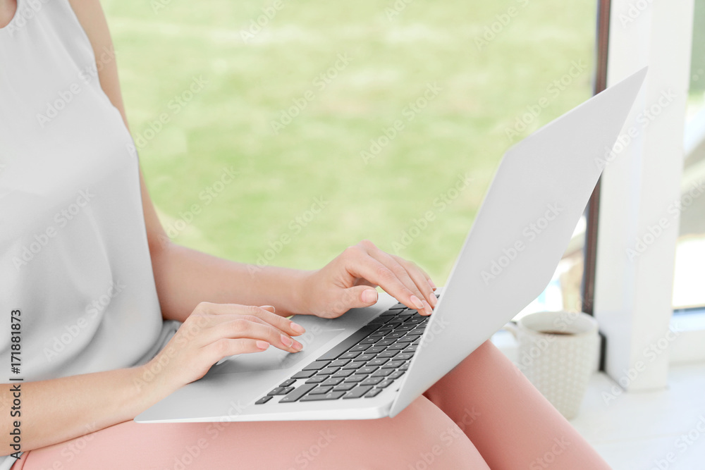 Young woman using laptop for searching information in internet on window sill Young woman using laptop for searching information in internet on window sill