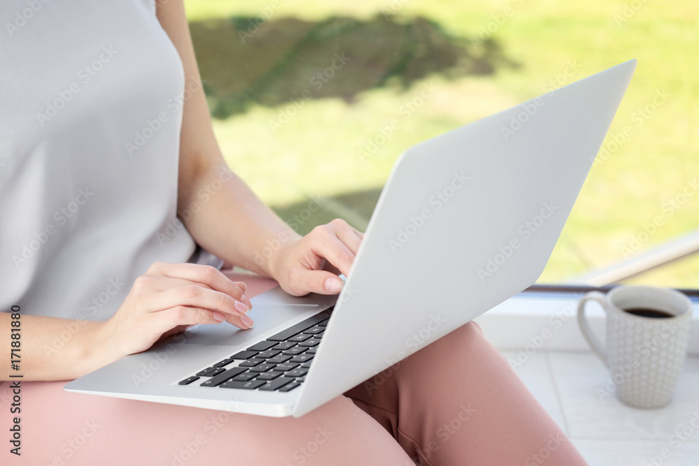 Young woman using laptop for searching information in internet on window sill Young woman using laptop for searching information in internet on window sill