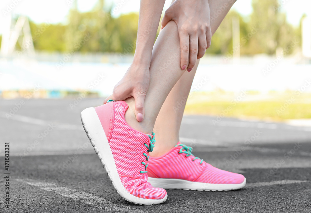 Young woman suffering from pain in leg, outdoors