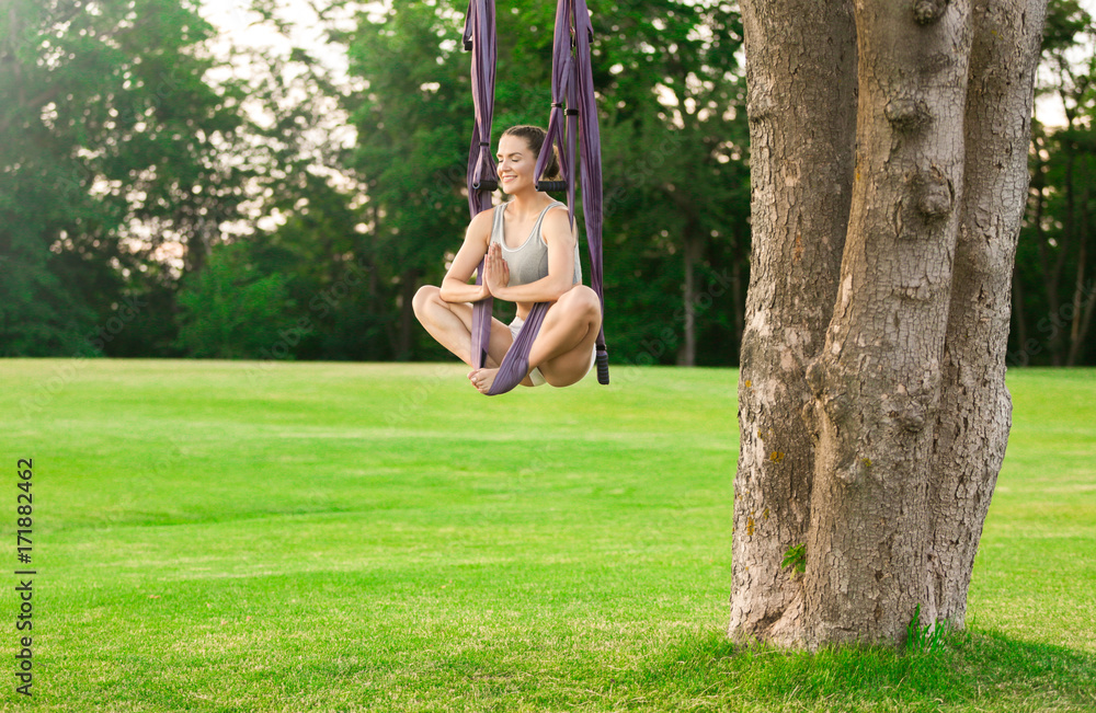 Young woman practicing aerial yoga on tree in park