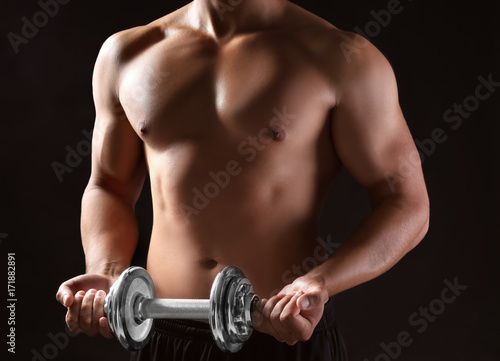 Sporty young man with dumbbell on dark background