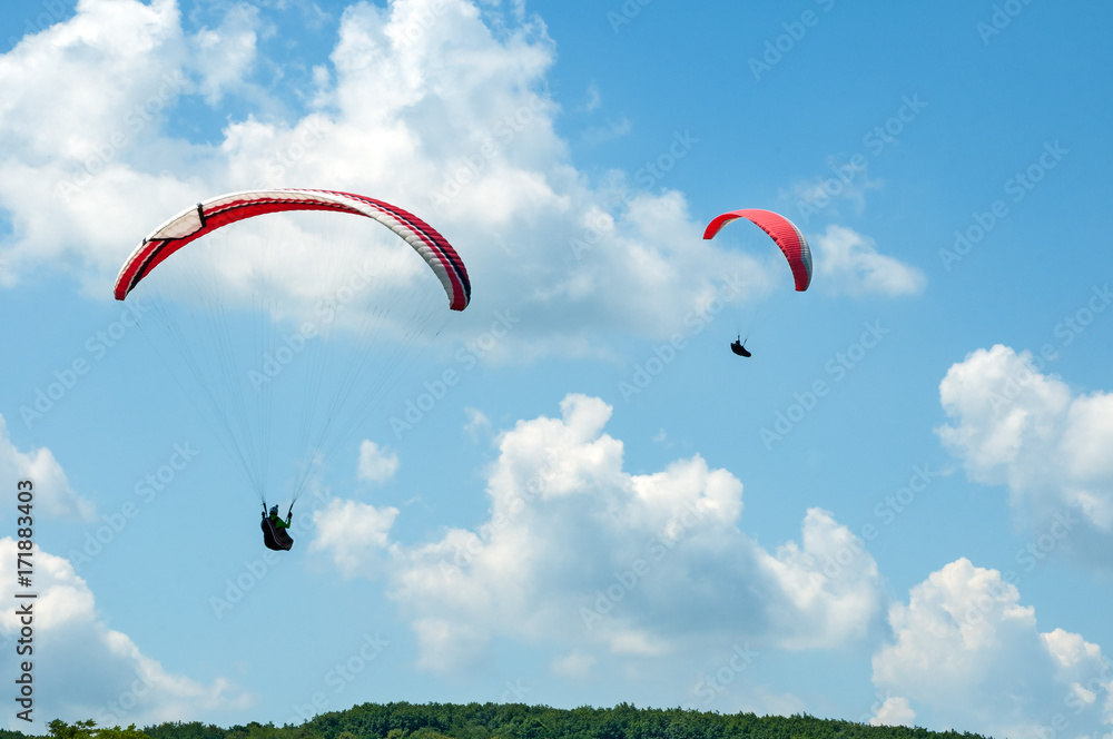 Two paragliders flying in the blue sky against the background of clouds. Paragliding in the sky on a sunny summer day. Two paragliders flying in the blue sky against the background of clouds. Paragliding in the sky on a sunny summer day.