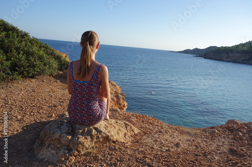 Tourist blonde girl looking at the beach Sa Caleta or Bou Nou in Ibiza island, Spain. 