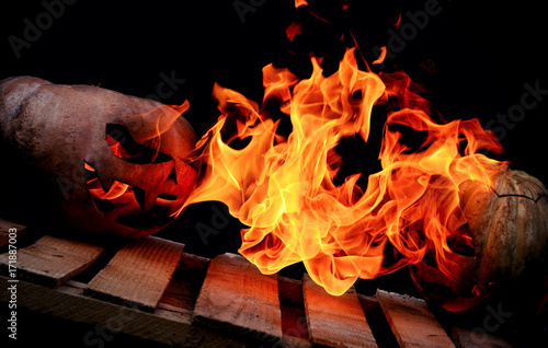 Two Very scary and dangerous Halloween pumpkins, with a menacing look and a smirk of a villain, in the darkness on a wooden pallet, attack each other with tongues of flame spewing them from within