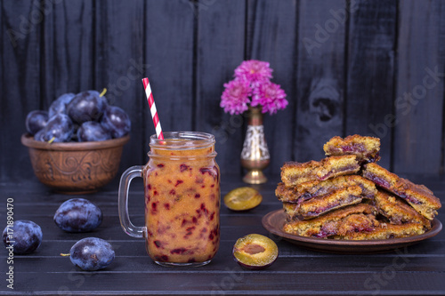 Homemade plum pie in plate, plum smoothies and raw plums on black wooden background