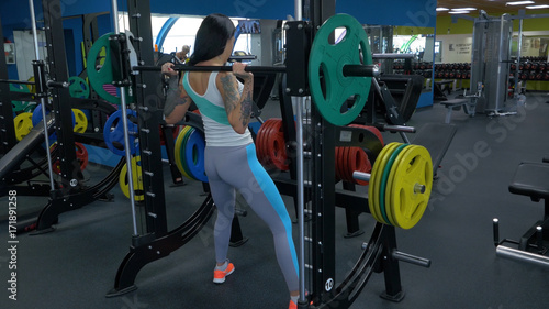 Beautiful girl exercising squatting with barbell. Sportive woman doing squatting with a barbell at the gym. Fit woman doing squat with barbell in the gym closeup