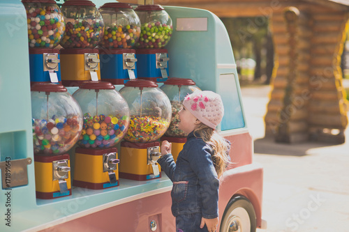 The little girl stopped in front of a battery of machines for the sale of small sweets. Genuinely enjoys opportunities to choose any treat Portrait of a girl in the Park on a walk. photo