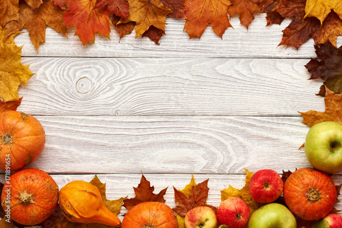 Autumn leaves, apples and pumpkins over wooden background