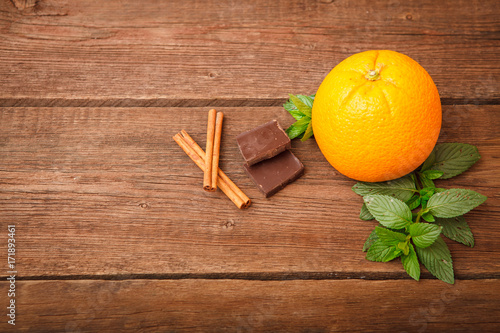 Fresh orange with melissa, chocolate and cinnamon on a wooden background. Space for text. Background.