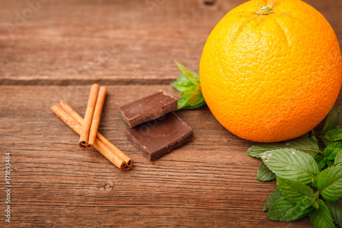 Fresh orange with melissa, chocolate and cinnamon on a wooden background. Space for text. Background.