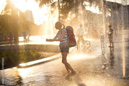 European tourist  with back pack washing hands in fountain water in Tirana city center square. water splashes in sunset back light