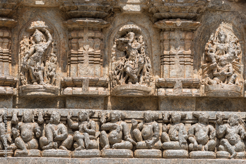Mysore, India - October 27, 2013: Stone frieze with heavily damaged statues on outside wall of central shrine, called Trikuta, at Chennakesave temple in somanathpur. Line of sitting men, deities.
