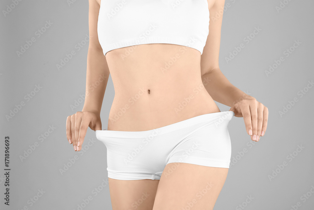 Fototapeta premium Young woman in underwear on gray background. Diet concept