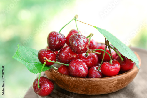 Wooden bowl with tasty ripe cherries on table outdoors