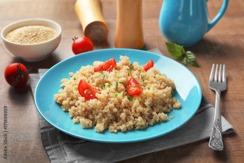 Plate with boiled quinoa grains on wooden table Plate with boiled quinoa grains on wooden table