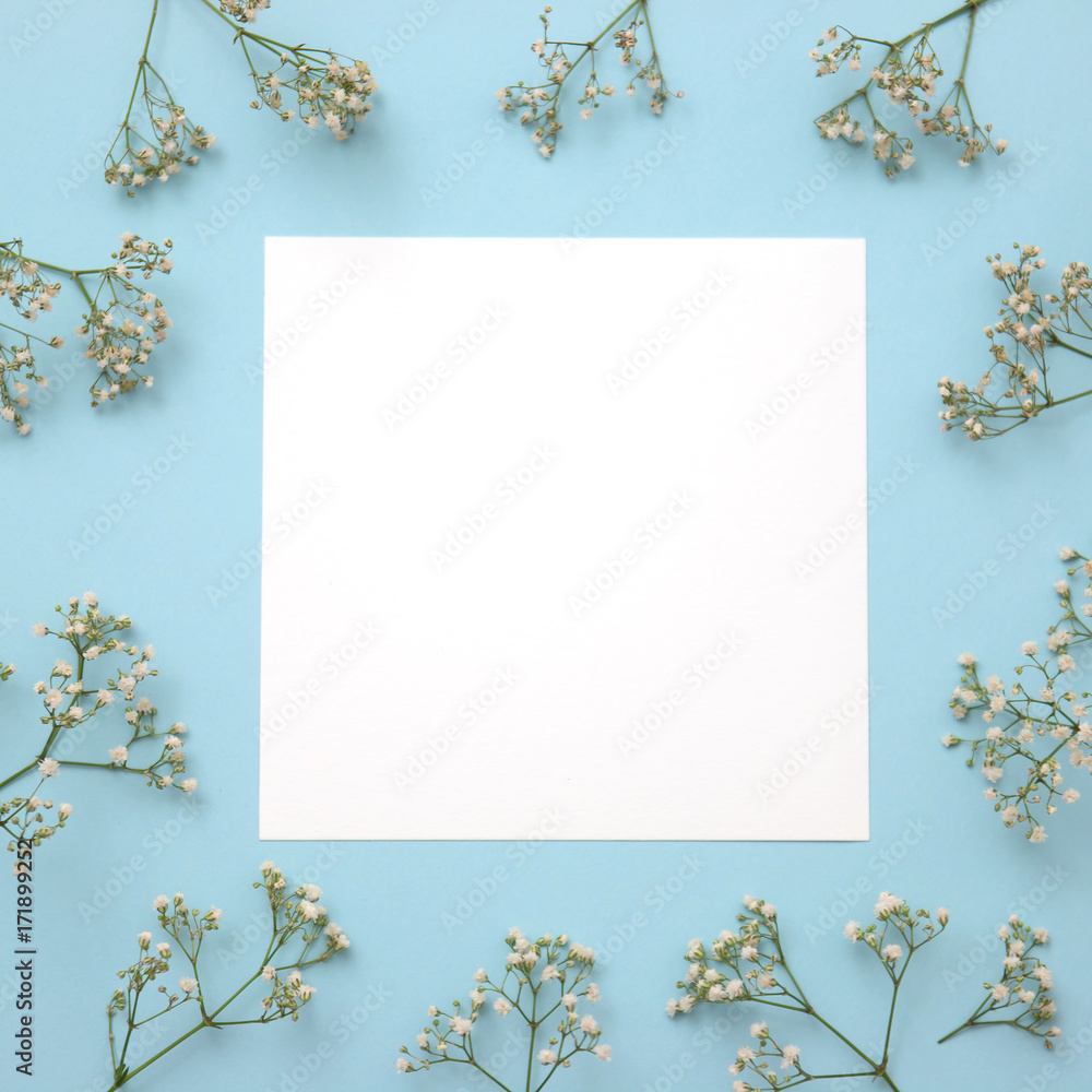 Creative layout made of flowers with paper card note on blue background. Flat lay. Nature concept