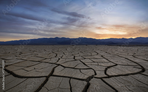 Sunset with clouds over a dry, cracked and scorched foreground photo
