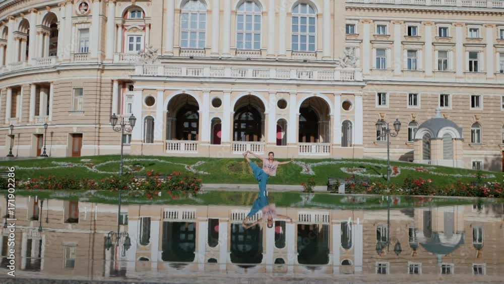 Reflection in the water of a sportive woman making stretching bent during workout in the city. Girl practicing yoga near fountain, beautiful architecture background. Slow motion. Reflection in the water of a sportive woman making stretching bent during workout in the city. Girl practicing yoga near fountain, beautiful architecture background. Slow motion.
