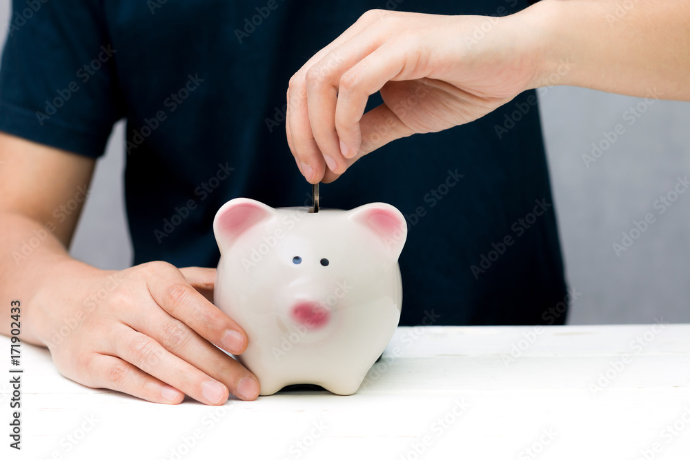 Human hand putting coin into a piggy bank. Saving concept. Human hand putting coin into a piggy bank. Saving concept.