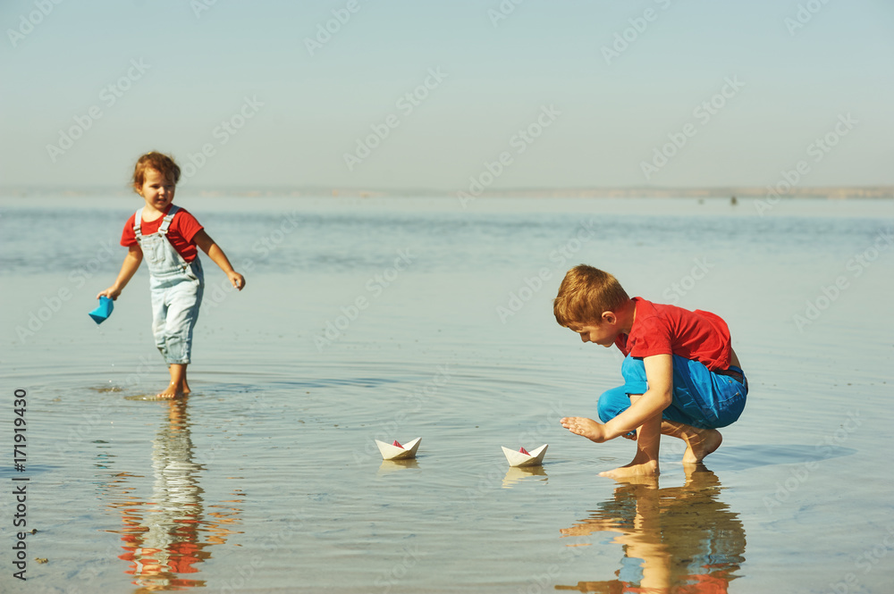 Cheerful children playing with paper boats . Brother and sister playing at the lake