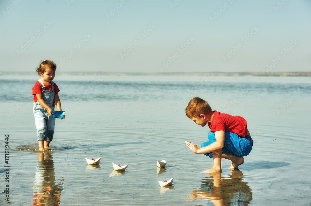 Cheerful children playing with paper boats . Brother and sister playing at the lake