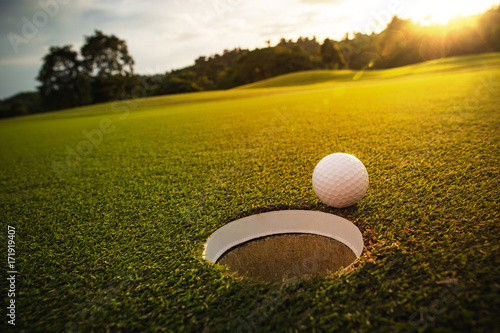 selektywna ostrość. biała piłka golfowa w pobliżu otworu na zielonej trawie, dobra na tle światła słonecznego i efektu flary