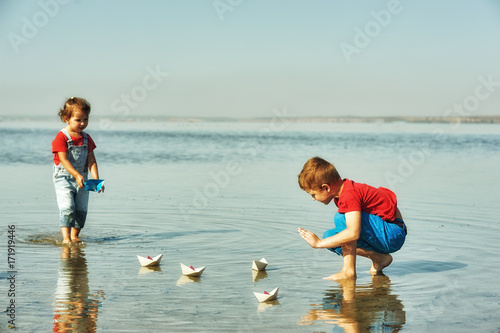 Cheerful children playing with paper boats . Brother and sister playing at the lake