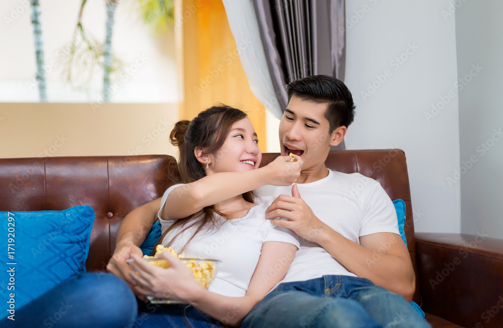 Young Asian couple in sweet moment, relax , laughting and eating popcorn to watching television in living room. Young Asian couple in sweet moment, relax , laughting and eating popcorn to watching television in living room.