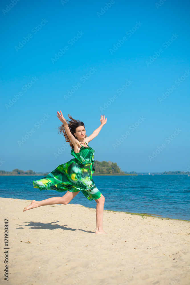 Woman wearing in green dress rest on a beach at warm day.  Mature thin lady Outdoors  on beach sand near water Landscape. Attractive Middle Aged Woman rest on nature