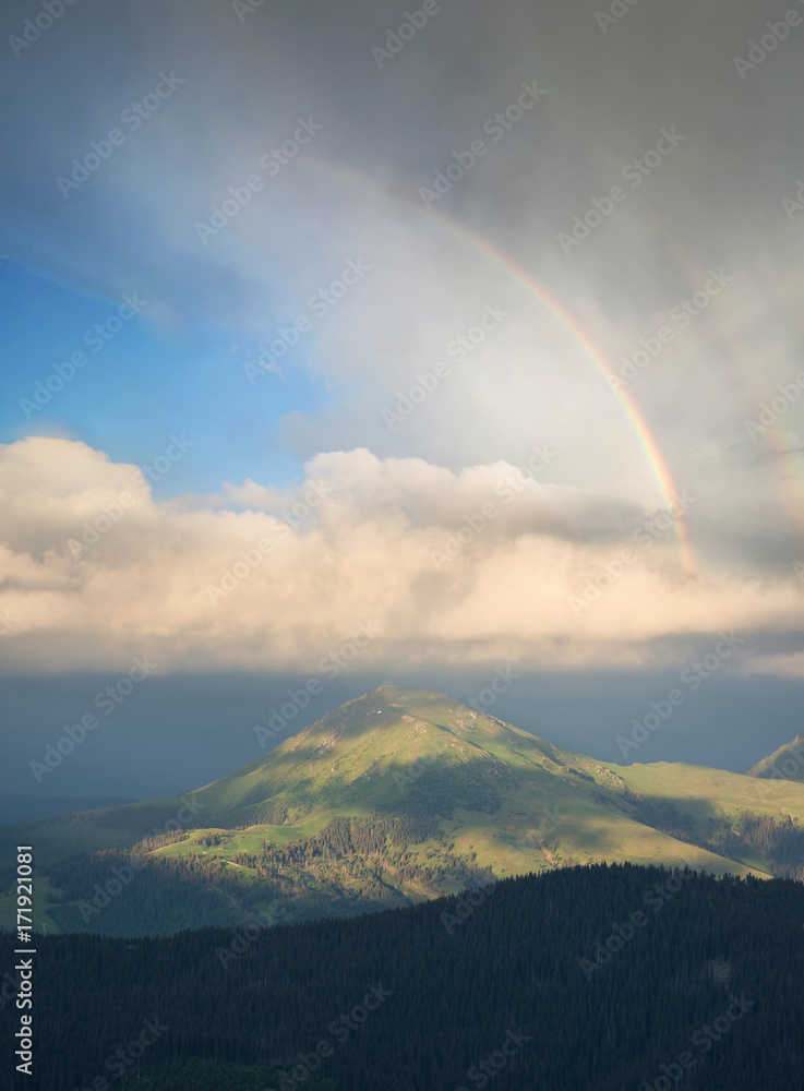 Rainbow under mountains at the rain. Beautiful natural landscape