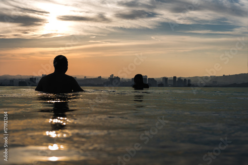 Man and woman in an infinity pool overlooking a busy city