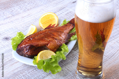Smoked fish and lemon on green lettuce leaves on Wooden cutting board and glass with beer isolated on white background. photo