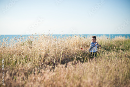 happy little boy running among the Golden fields of rye on sea background