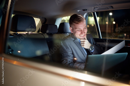 smiling businessman in moving car working on his laptop. © luckybusiness