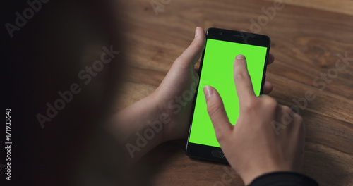 female teen girl using smartphone with green screen over wood table
