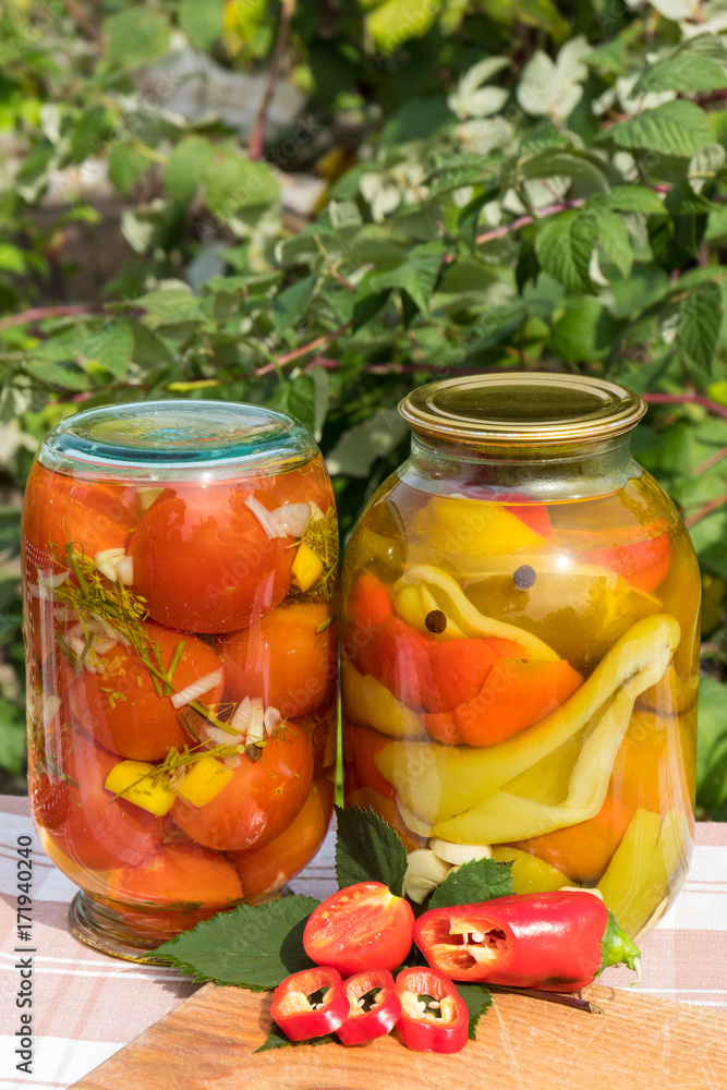 Banks with canned tomatoes and peppers in the oil. On the background of the garden. Banks with canned tomatoes and peppers in the oil. On the background of the garden.