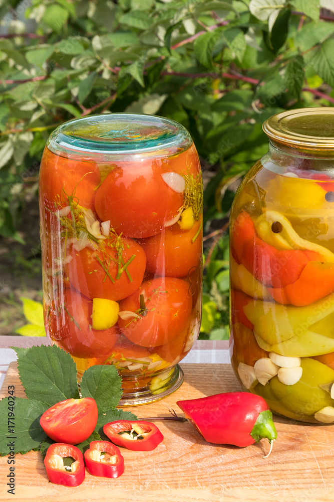Banks with canned tomatoes and peppers in the oil. On the background of the garden. Banks with canned tomatoes and peppers in the oil. On the background of the garden.
