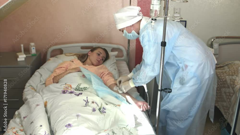 Skillful general practitioner is putting dropper in hospital. Young woman doctor anesthesiologist puts the dropper in hospital room, nurse puts the patient medical drip into a vein Skillful general practitioner is putting dropper in hospital. Young woman doctor anesthesiologist puts the dropper in hospital room, nurse puts the patient medical drip into a vein