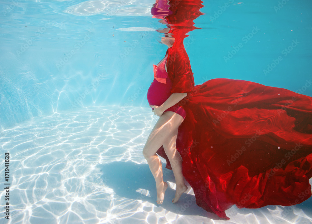 Foto de Pregnant woman swim, dive, pose underwater in swimming pool with red fabric. Aqua