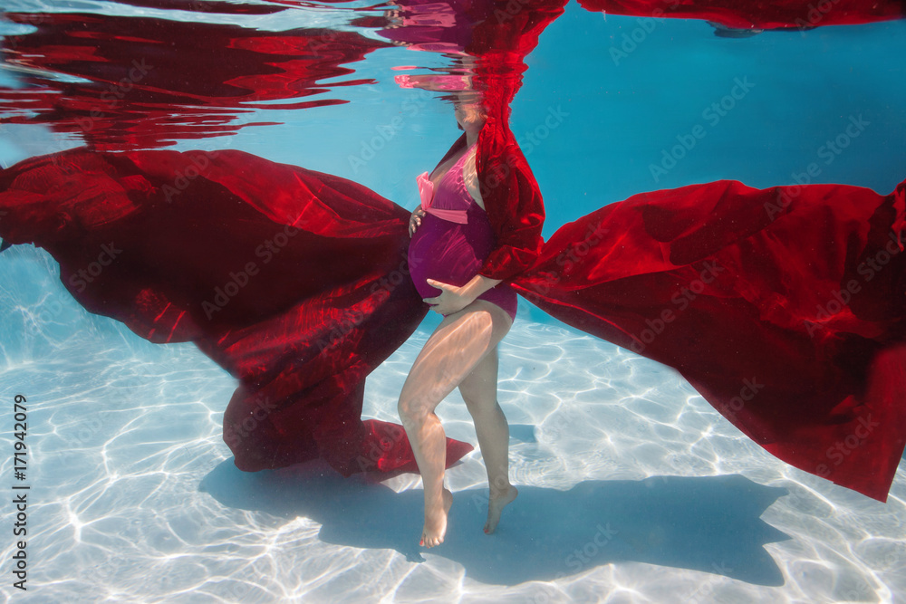 Pregnant woman swim, dive, pose underwater in swimming pool with red