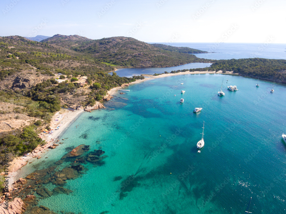Aerial drone view of Rondinara Bay with sailing boats and people swimming at the sunny beach