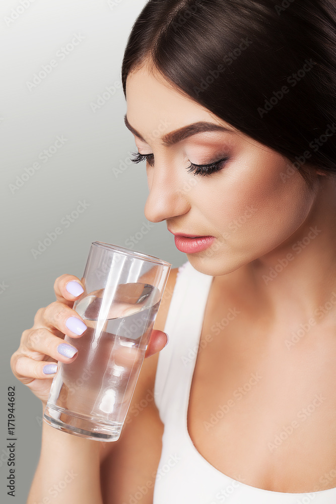 Young girl drinks water. Healthy look of the face. Portrait of a girl. The concept of beauty and health. On a gray background. Young girl drinks water. Healthy look of the face. Portrait of a girl. The concept of beauty and health. On a gray background.