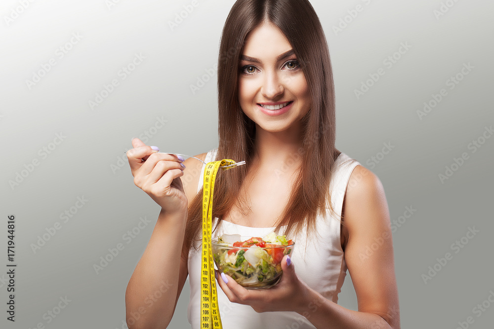 Healthy Lifestyle. A woman eats a salad. Young woman eating healthy food. Diet. Beautiful and healthy woman. The concept of health and beauty. On a gray background. Healthy Lifestyle. A woman eats a salad. Young woman eating healthy food. Diet. Beautiful and healthy woman. The concept of health and beauty. On a gray background.