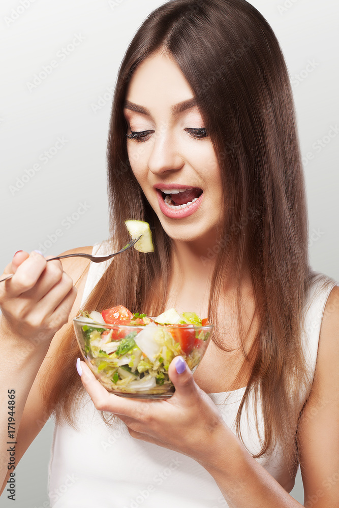 Portrait of a young woman eating a salad. Healthy lifestyle with green meals. Diet and Sports. The concept of health and beauty. On a gray background. Portrait of a young woman eating a salad. Healthy lifestyle with green meals. Diet and Sports. The concept of health and beauty. On a gray background.